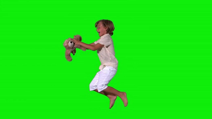 可爱的男孩在绿色背景上跳跃和捕捉泰迪