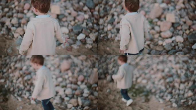 可爱的小男孩在石头附近的沙滩上奔跑，从1英尺转移到另一个。男性在外面散步