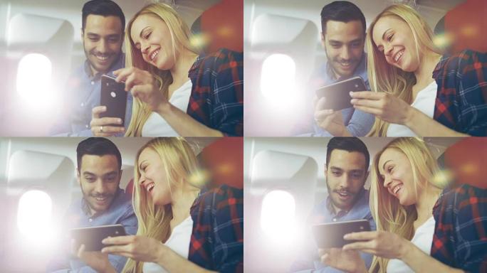 在商用飞机上，漂亮的年轻金发女郎与英俊的西班牙裔男性在智能手机上观看视频并微笑。阳光透过飞机的窗户照