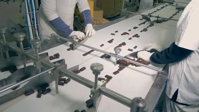 巧克力糖果的俯视图由工人分类并沿着传送带进一步移动