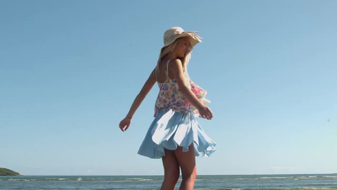 迷人的金发女郎戴着草帽在海滩上旋转