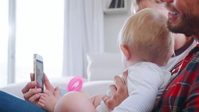 年轻的白人夫妇和他们的婴儿一起使用智能手机