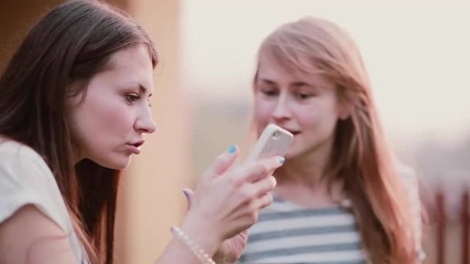 两个漂亮的女人正在使用智能手机并进行对话。朋友在夏天的户外手机上观看照片