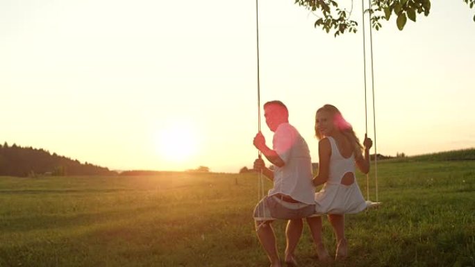 慢动作: 可爱的年轻微笑夫妇在大自然的夏日日落中摇摆