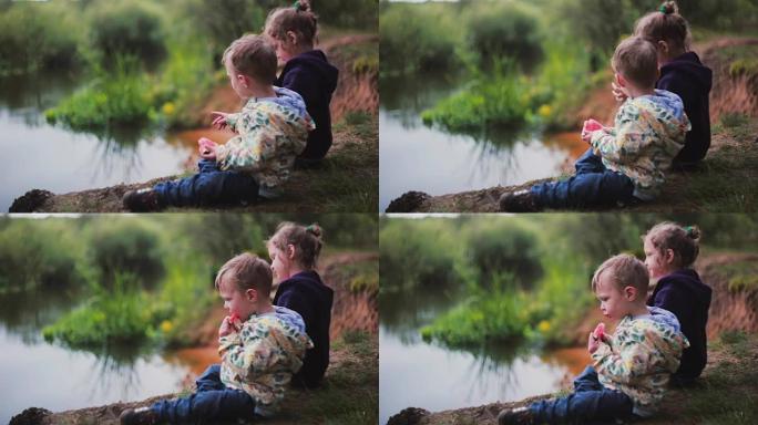 两个可爱的小孩的侧视图，一个男孩和一个女孩，吃西瓜，坐在河岸上