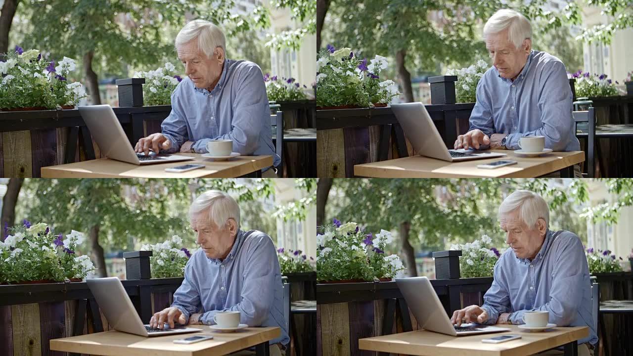 老人在户外咖啡馆的笔记本电脑上工作