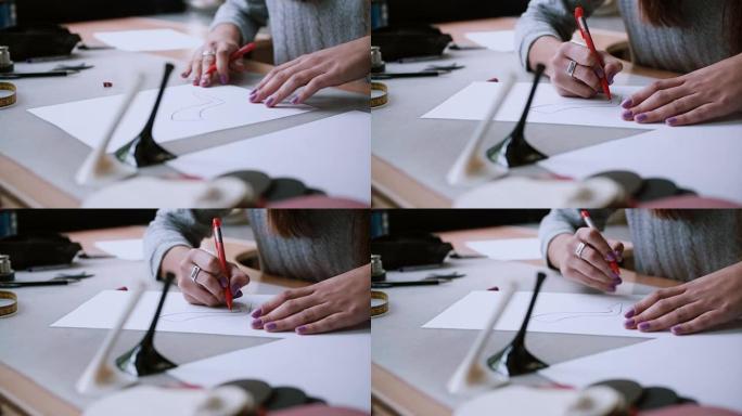 年轻女子手的特写。女孩坐在桌子旁，用铅笔在纸上画鞋子的草图。4K