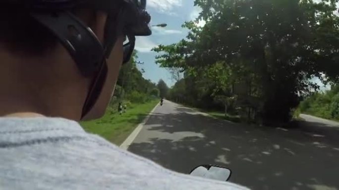 POV: 坐在年轻的男司机后面的踏板车上，沿着狭窄的异国情调的道路骑行。