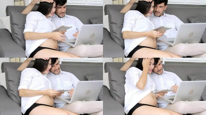 孕妇和丈夫在沙发上使用笔记本电脑。高清格式。
