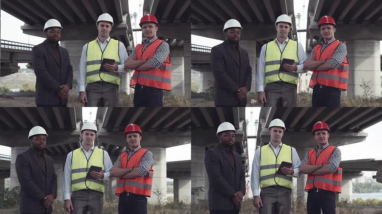 三个建筑师戴着防护帽看着摄像机