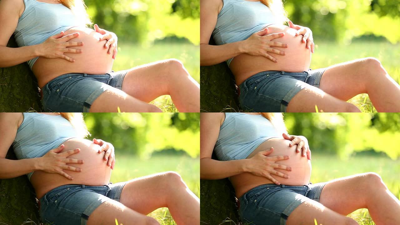 孕妇抚摸着她的小肚子坐在树上
