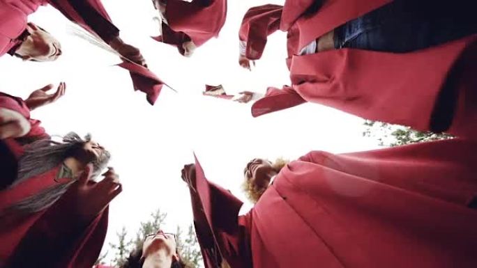 女生和男生的低角度镜头即将毕业的学生向天空投掷灰泥板并大笑。庆祝毕业、传统服装和教育理念。