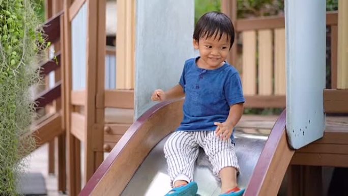 SLO MO开朗的亚洲小男孩从儿童滑梯上走下来。