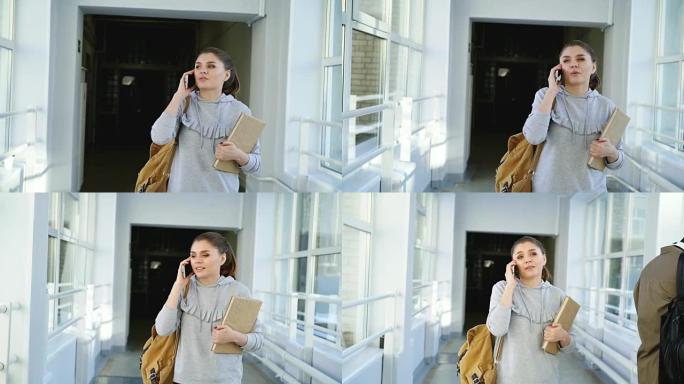 多莉拍摄了美丽漂亮的女学生走在大学走廊上，拿着课本在窗户附近路过的外国学生的电话聊天