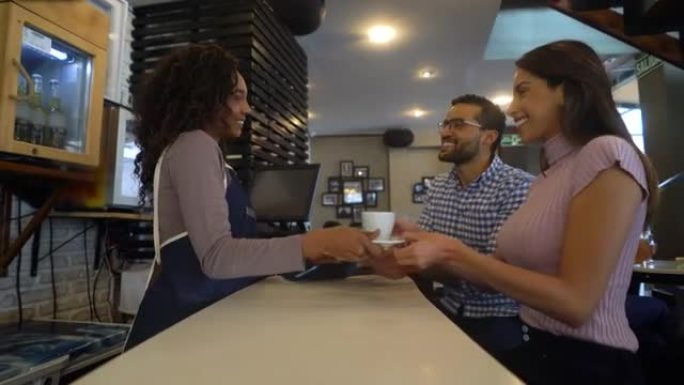 女服务员为坐在酒吧柜台的一对夫妇提供咖啡，他们都微笑着