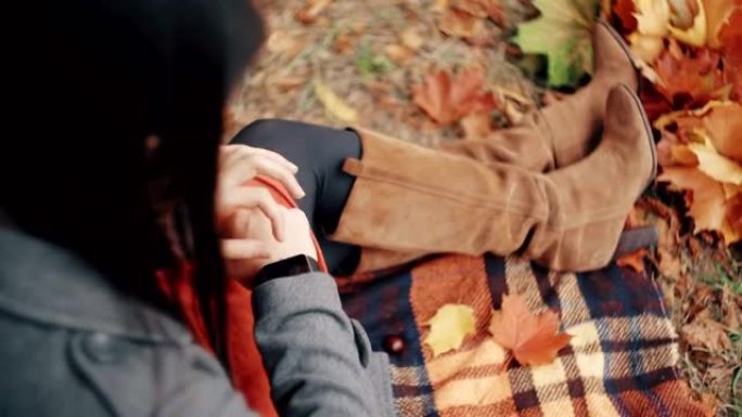 美丽、时尚、年轻的女人在秋季公园使用坐在格子上的智能时钟。全高清