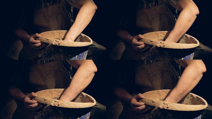 男性陶艺家的手在装有粘土的桶内缓慢移动。