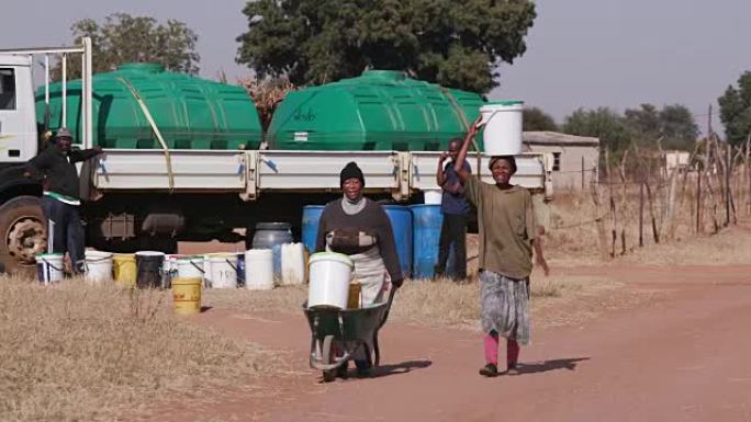 两名非洲妇女从油轮上取水，然后走回自己的家