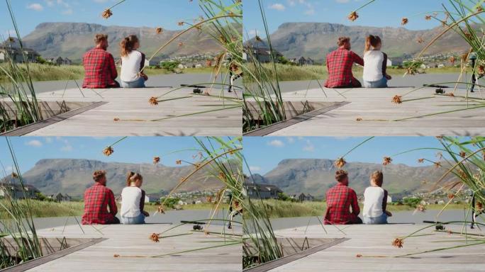 夫妇坐在湖边和山边的码头上，后视图