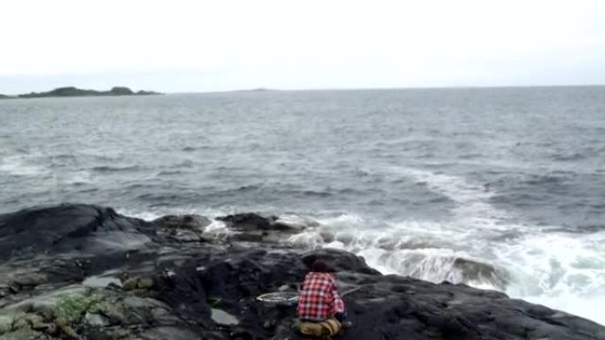 男子背包客旅行者在多岩石的海岸上休息。无人机的观点