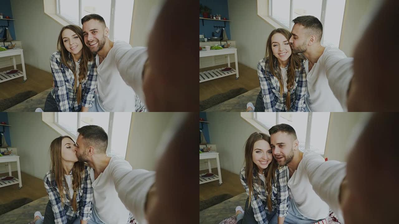 年轻微笑和美丽的夫妇的POV在智能手机相机上自拍，早上坐在床上亲吻