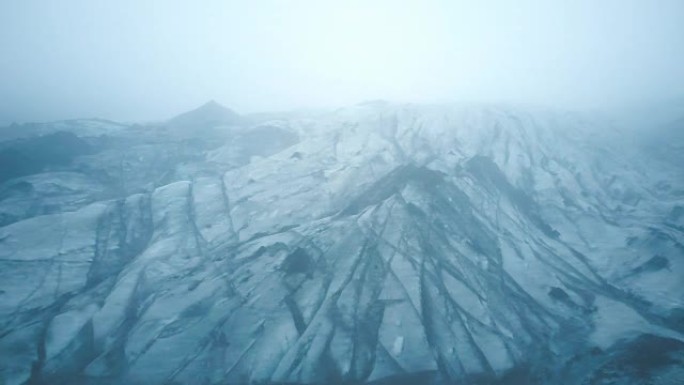 冰岛黑灰白色冰川Myrdalsjokull的鸟瞰图。直升机在雾中飞越冰山