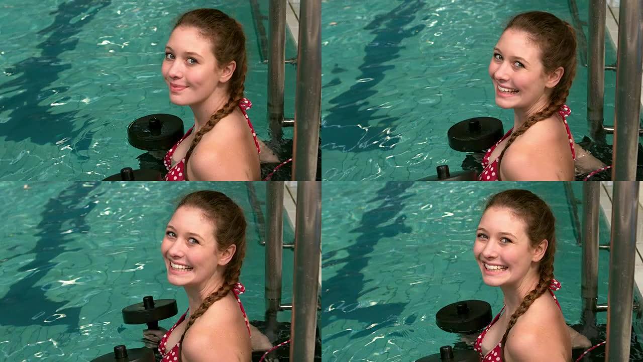 健康的女人在游泳池里举重，对着镜头微笑