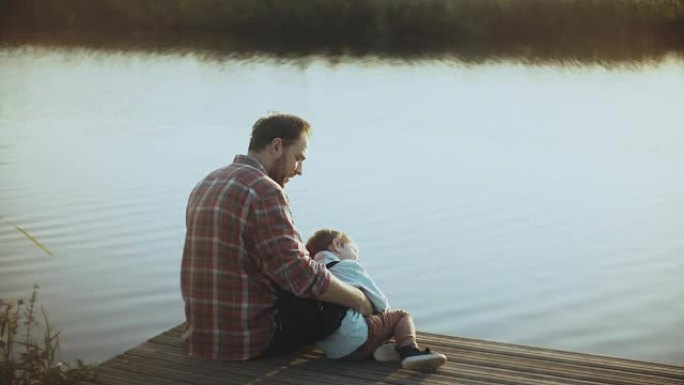 白人男子和小男孩坐在湖码头上。父子在一起。幸福的关系。抚养孩子。4K