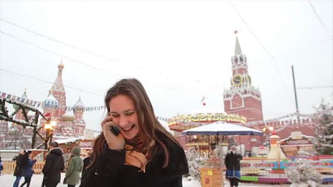 冬日里，一名女子站在莫斯科红场上，克里姆林宫和圣巴西尔大教堂前打电话
