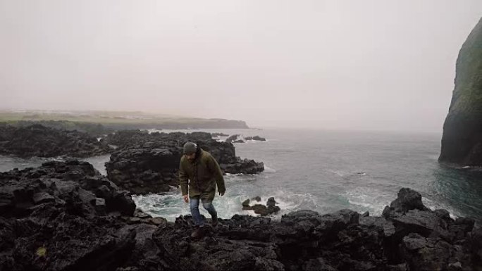 年轻英俊的男人在阴天穿过海边的岩石。游客探索新的地方