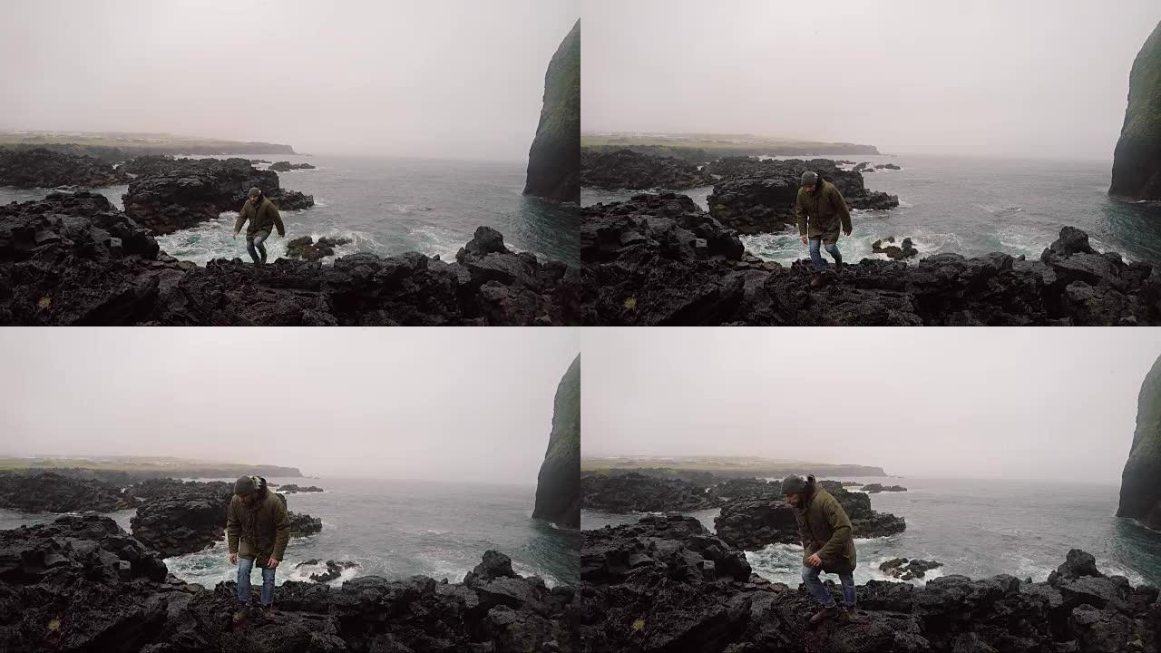 年轻英俊的男人在阴天穿过海边的岩石。游客探索新的地方