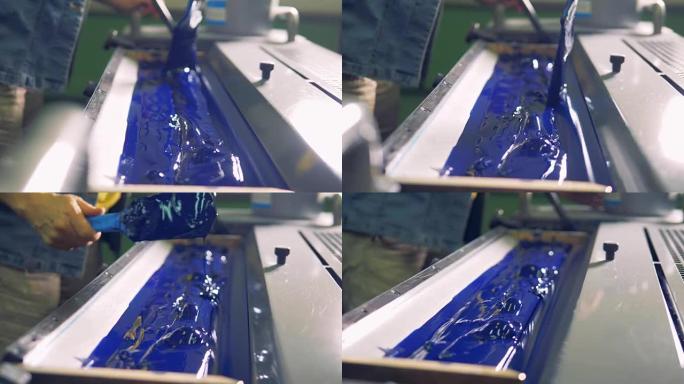 一名男子在工厂印刷机的特殊单元中铺设了厚厚的蓝色油漆。