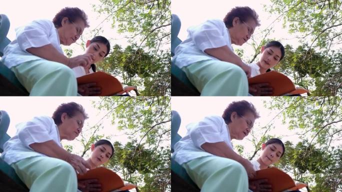 照顾老人一个女孩 (女人) 和祖母坐在平装本上看书，在公园里。概念寄宿房、疗养院、老人之家、老人帮助