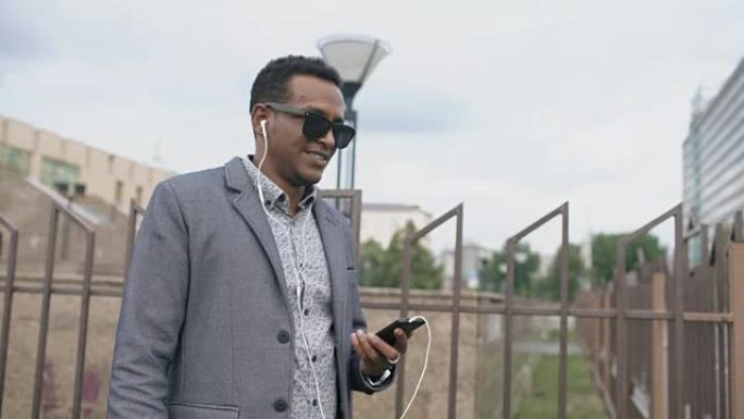 Steadicam拍摄了年轻的混血商人在户外听智能手机上的音乐