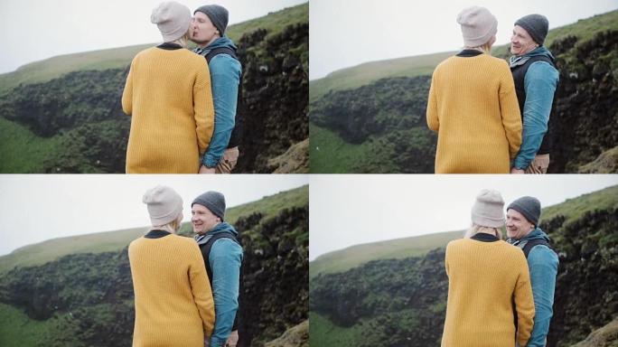 年轻美丽的夫妇站在山上说话，接吻。探索自然的旅游男女