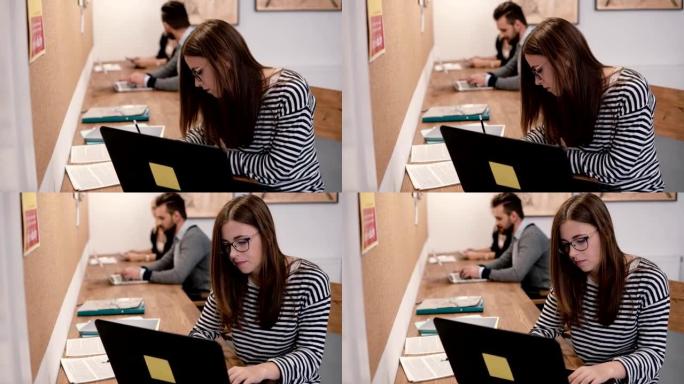 年轻迷人的女孩正在使用笔记本电脑，处理文件，在现代创业办公室做笔记