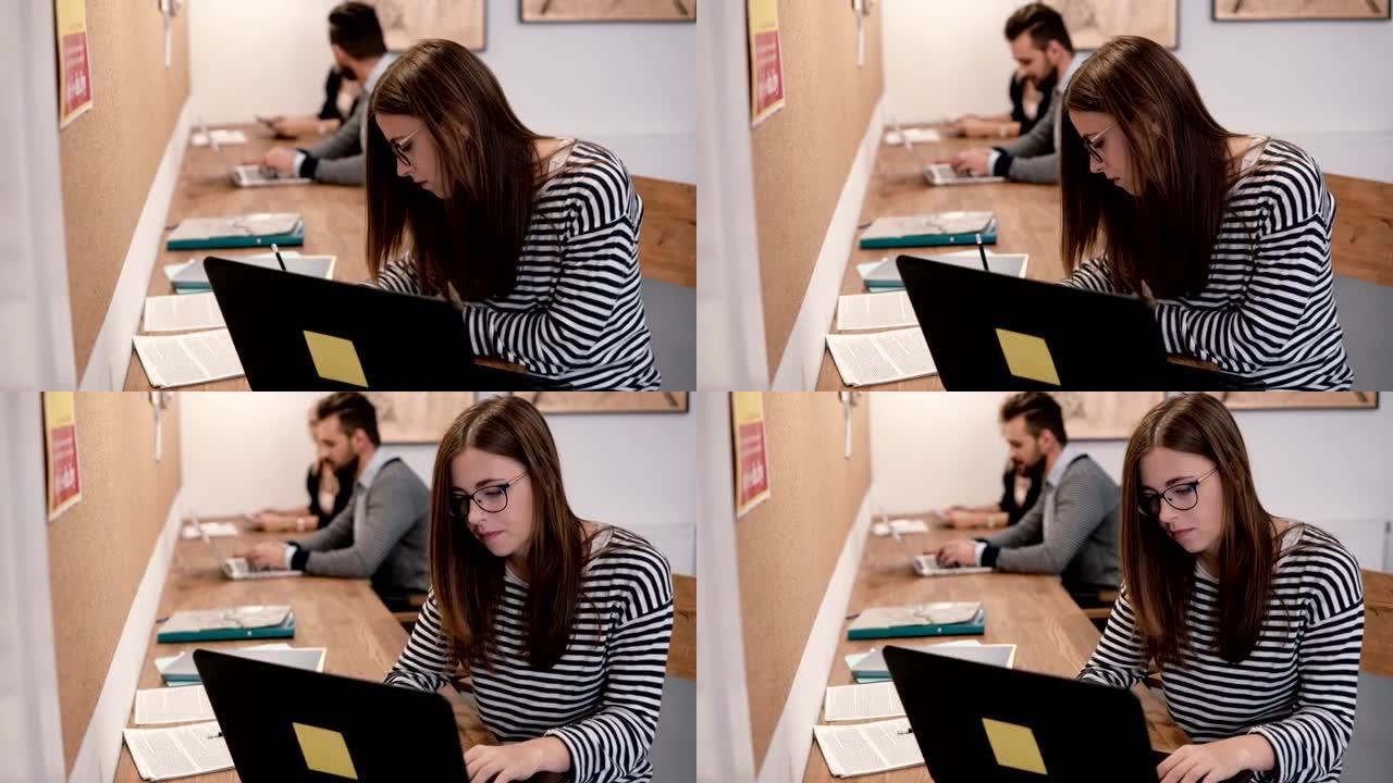 年轻迷人的女孩正在使用笔记本电脑，处理文件，在现代创业办公室做笔记