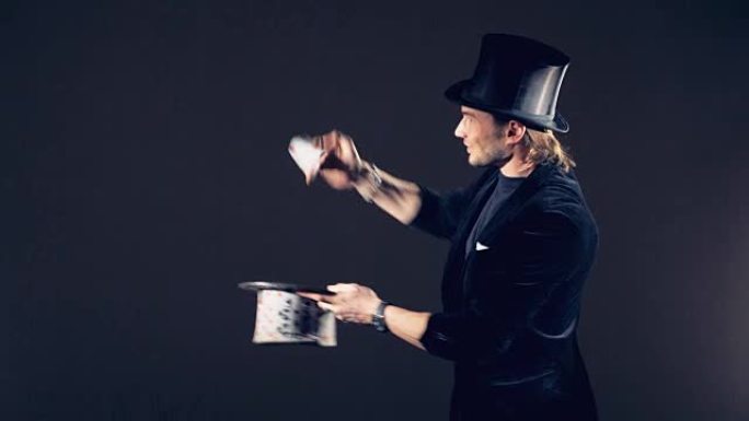一位男性魔术师正在用纸牌表演魔术，并将它们放在一起制成纸牌礼帽