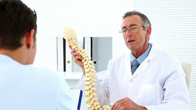 成熟的医生和他的病人谈论脊柱模型