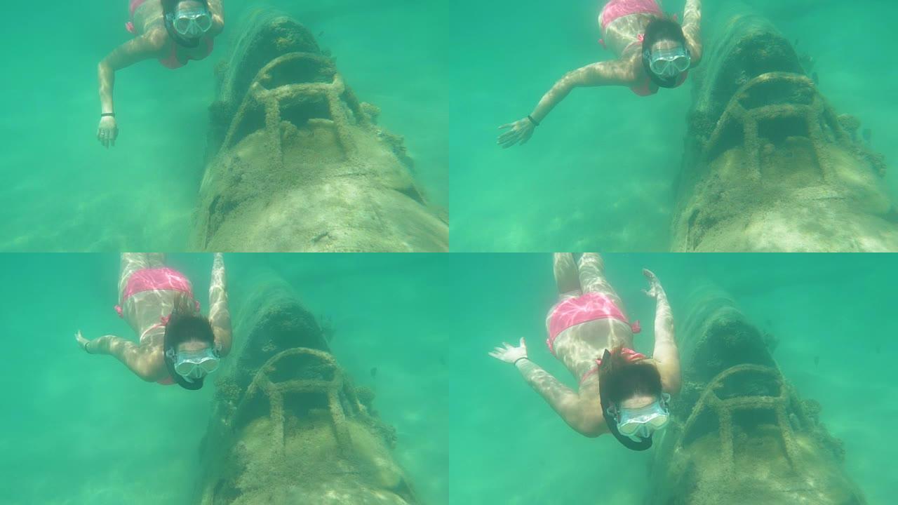 水下: 年轻的女性浮潜者好奇地看着腐烂的飞机驾驶舱