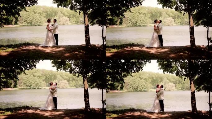 婚礼当天的恋人站在河岸上，互相看着对方，亲吻。穿着漂亮连衣裙的快乐新娘