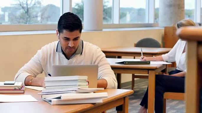 年轻的印度男大学生在校图书馆使用笔记本电脑