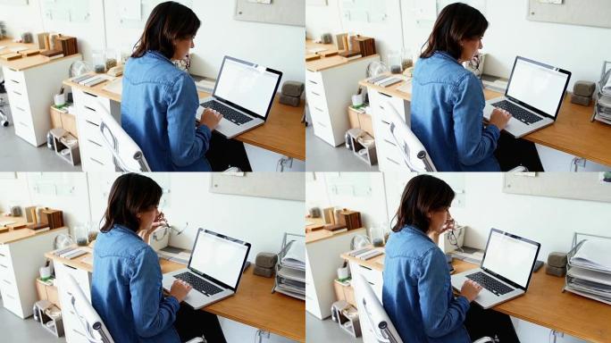 女性高管坐在办公桌前并使用笔记本电脑