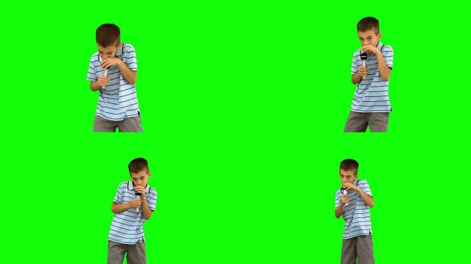 小男孩拿着麦克风在绿屏上唱歌