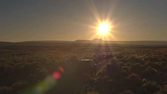 空中: 黑色SUV汽车在金色日落时驶过无尽的浓密沙漠