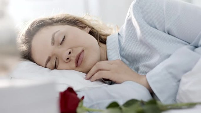 男人手把玫瑰放在枕头上，而女人睡在旁边