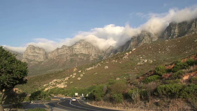 南非以12个使徒山为背景的道路上经过的汽车
