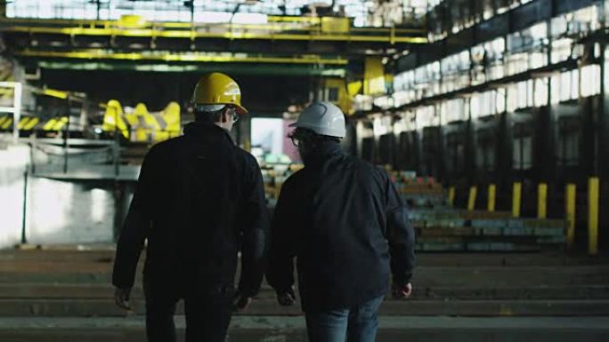 两名工人戴着安全帽，带着起重机在工业区行走。