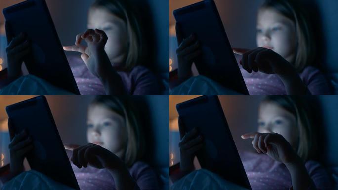 晚上在床上可爱的小女孩与平板电脑互动。