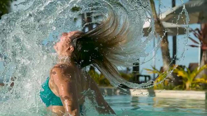 特写: 豪华泳池中的女孩翻转头发，并在身后喷洒池水。